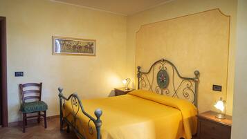 A bedroom with a bed, a chair, a nightstand, a lamp, and a wall-mounted picture.