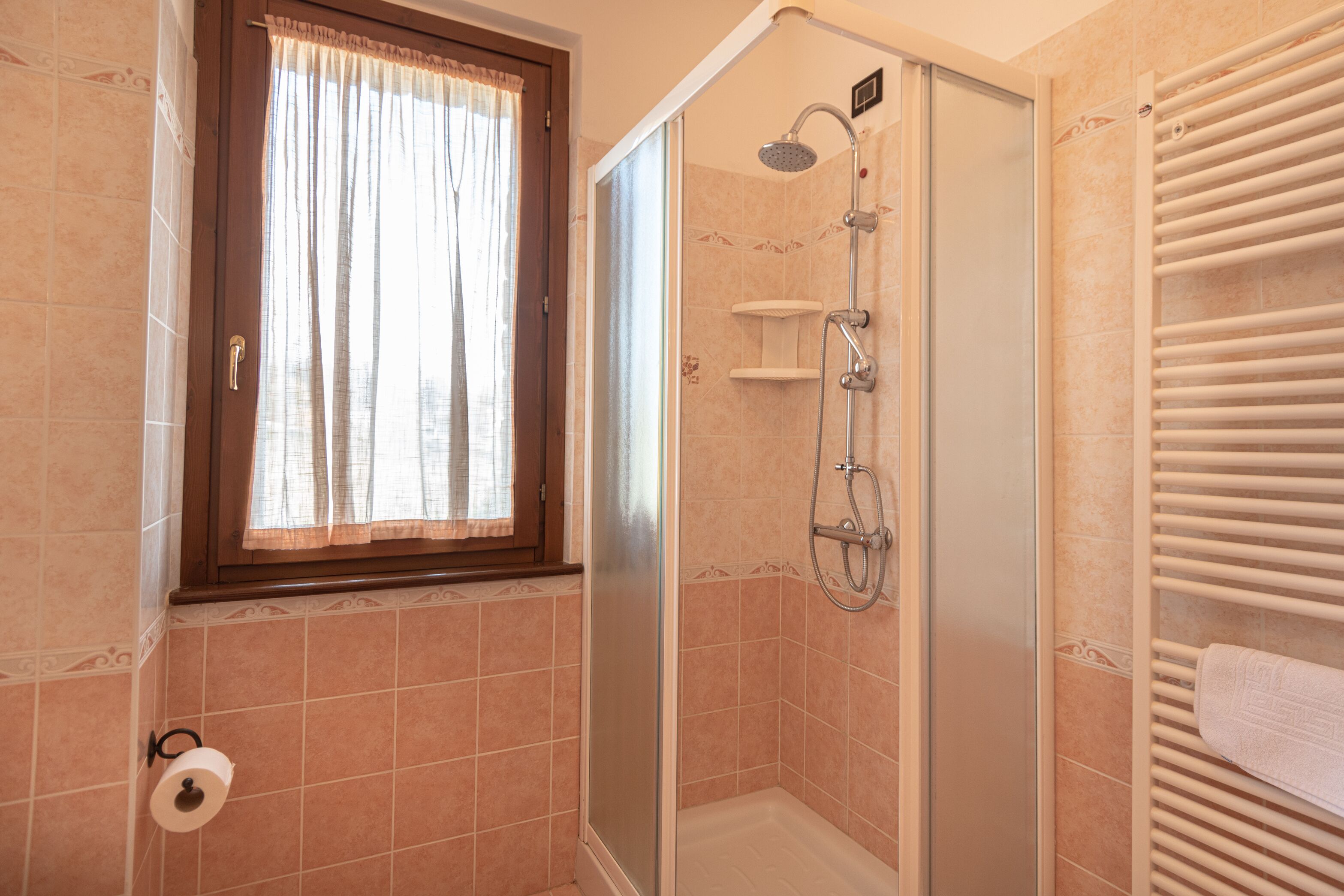 Eine Dusche mit Glastür, einem Handtuchhalter und einem fenster mit Vorhängen.