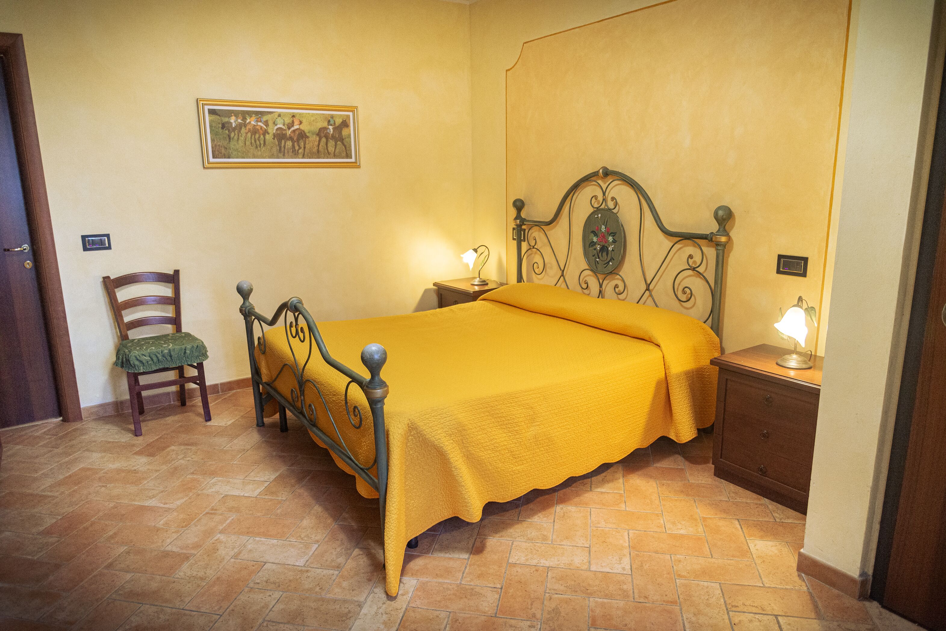 A bedroom with a bed, a chair, a nightstand, and a wall-mounted picture.