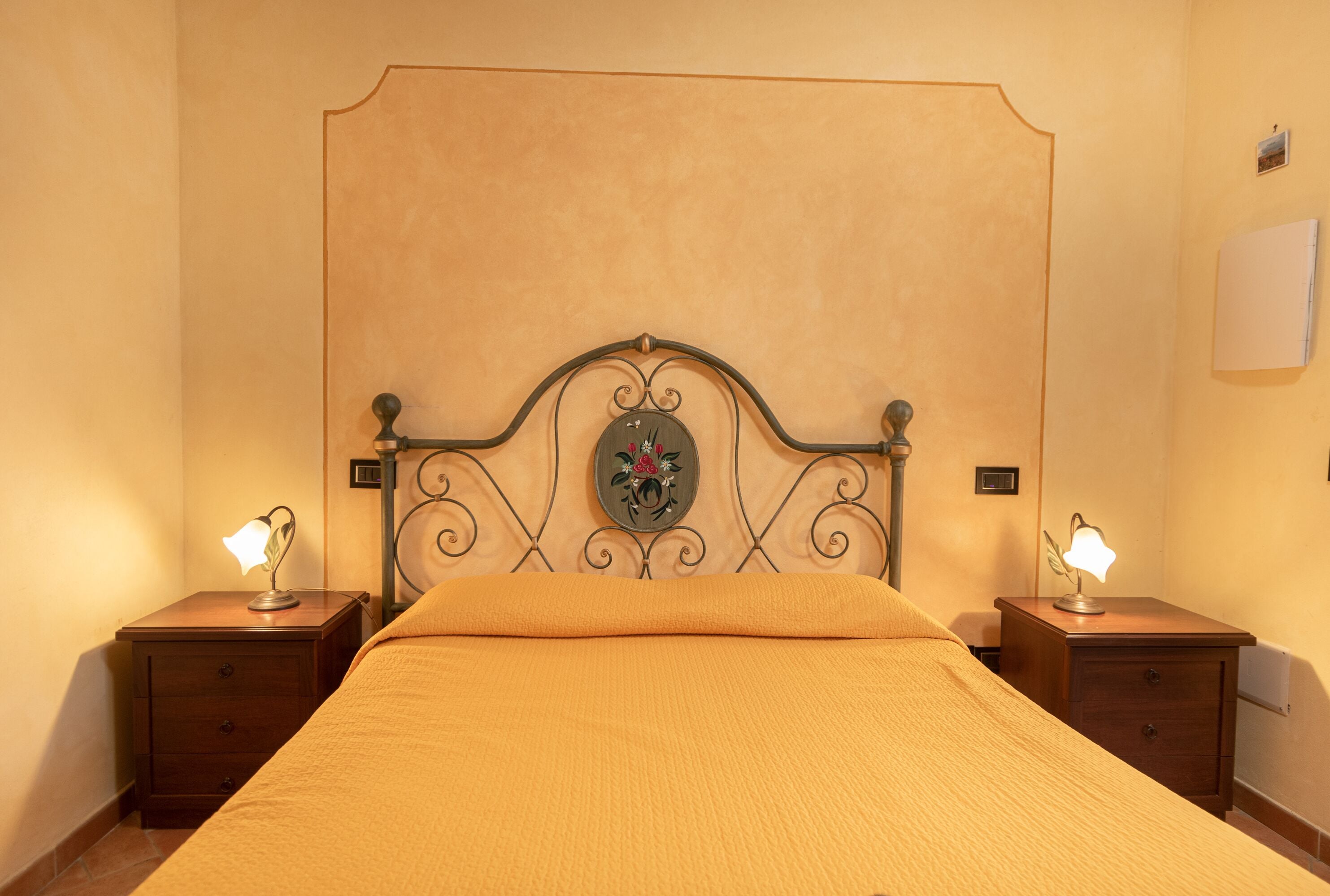 A neatly made bed with a headboard, two bedside tables with lamps, and a wall-mounted light switch.