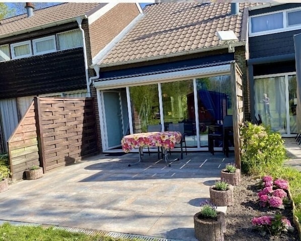 A patio with a table and chairs, a brick wall, and a garden with plants.