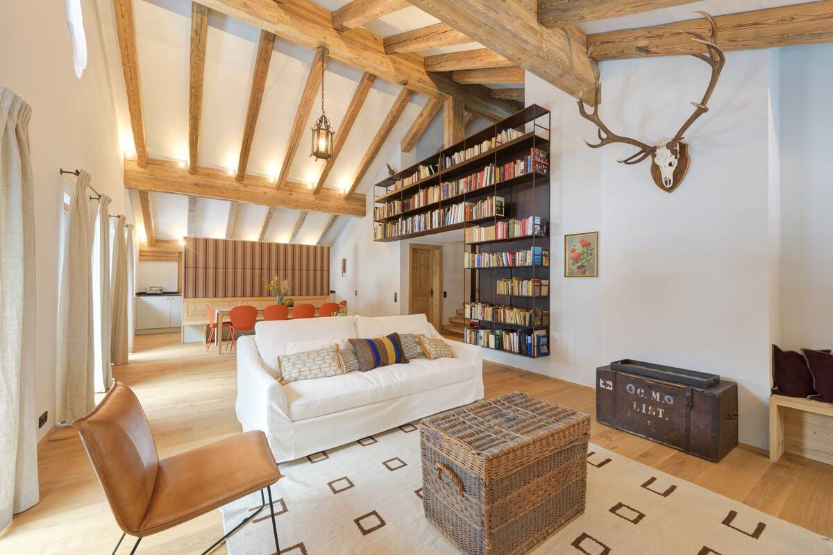 Un salon spacieux avec un canapé blanc, un plafond en bois et une bibliothèque remplie de livres.