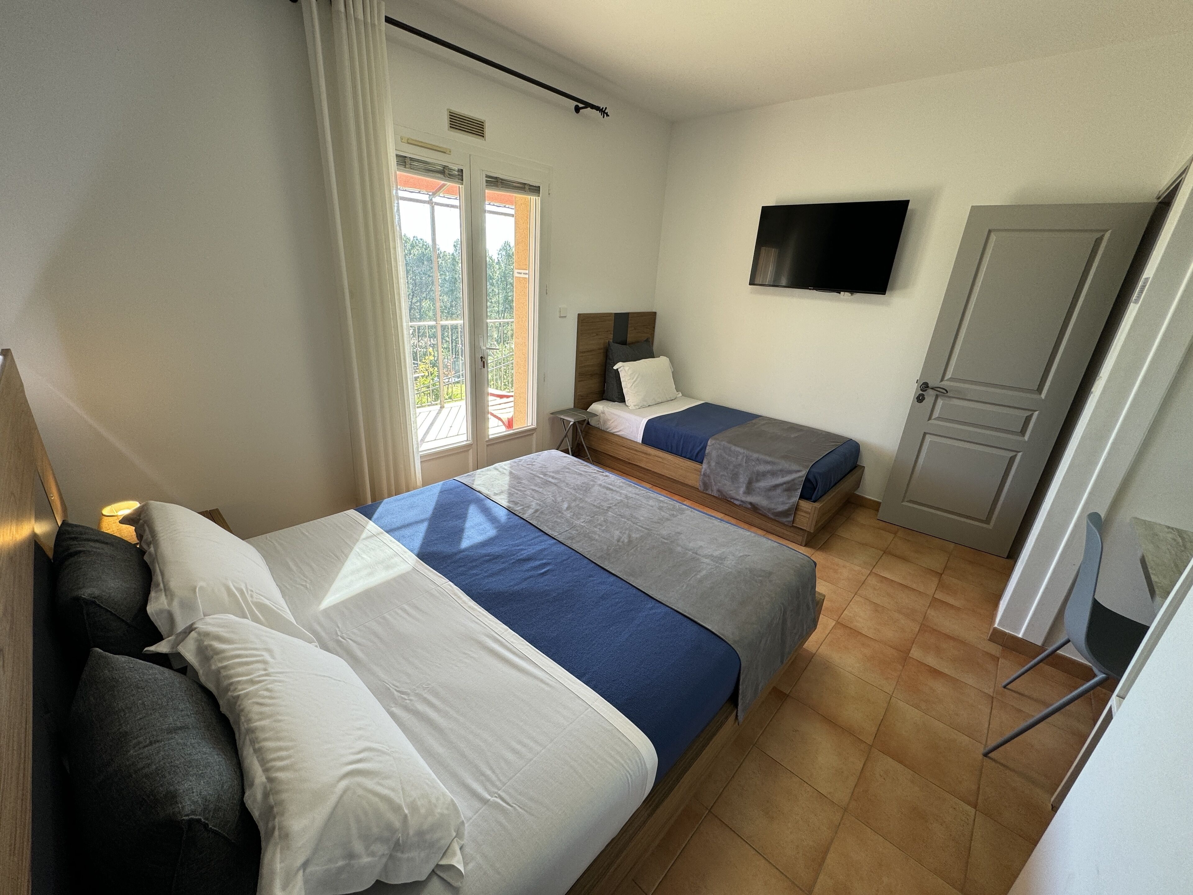 Habitación de hotel con dos camas, televisión, puerta y ventana con cortinas.