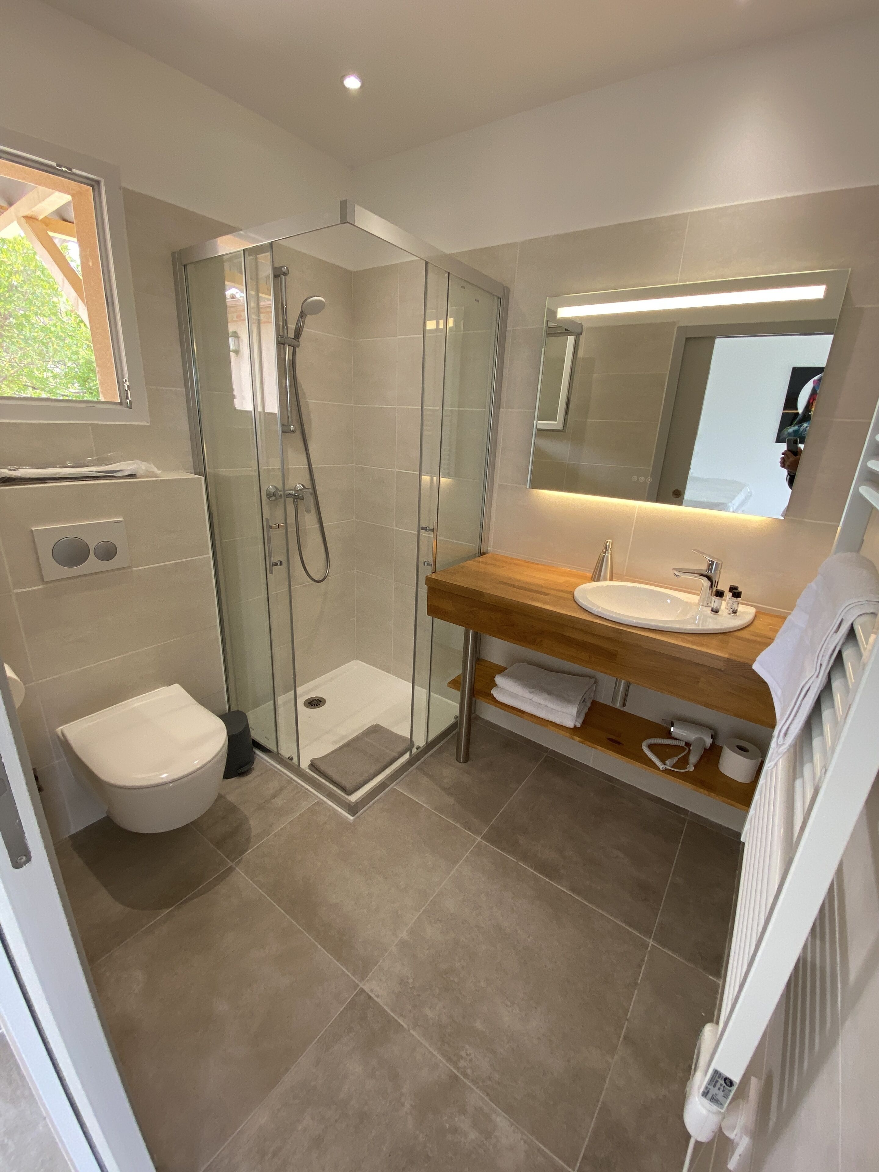 Een moderne badkamer met een glazen douchecabine, een houten wastafelmeubel en een wit toilet.
