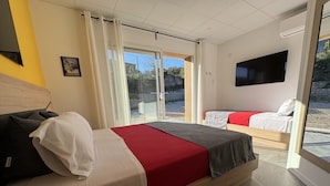 Une chambre d’hôtel moderne dotée d’un grand lit, d’un lit plus petit, d’une télévision et d’une porte-fenêtre coulissante donnant sur l’extérieur.