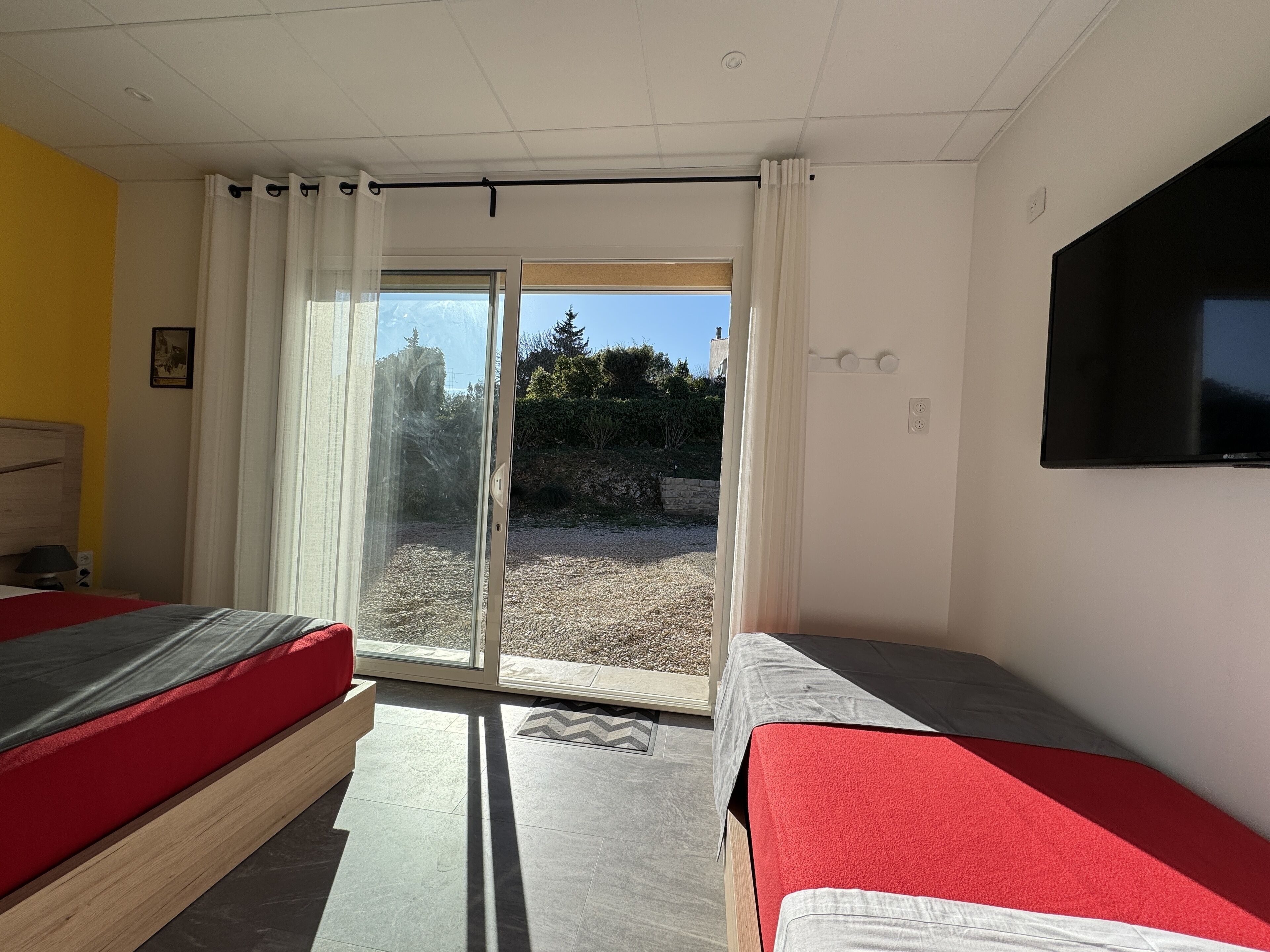 A hotel room with two beds, a TV, and a sliding glass door leading to an outdoor area.