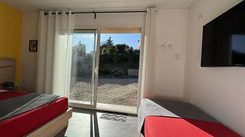 A hotel room with two beds, a TV, and a sliding glass door leading to an outdoor area.