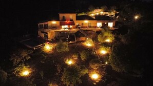 Une maison à deux étages dotée d’un espace extérieur aménagé et couvert, entourée d’arbres et éclairée par des luminaires encastrés dans le sol.