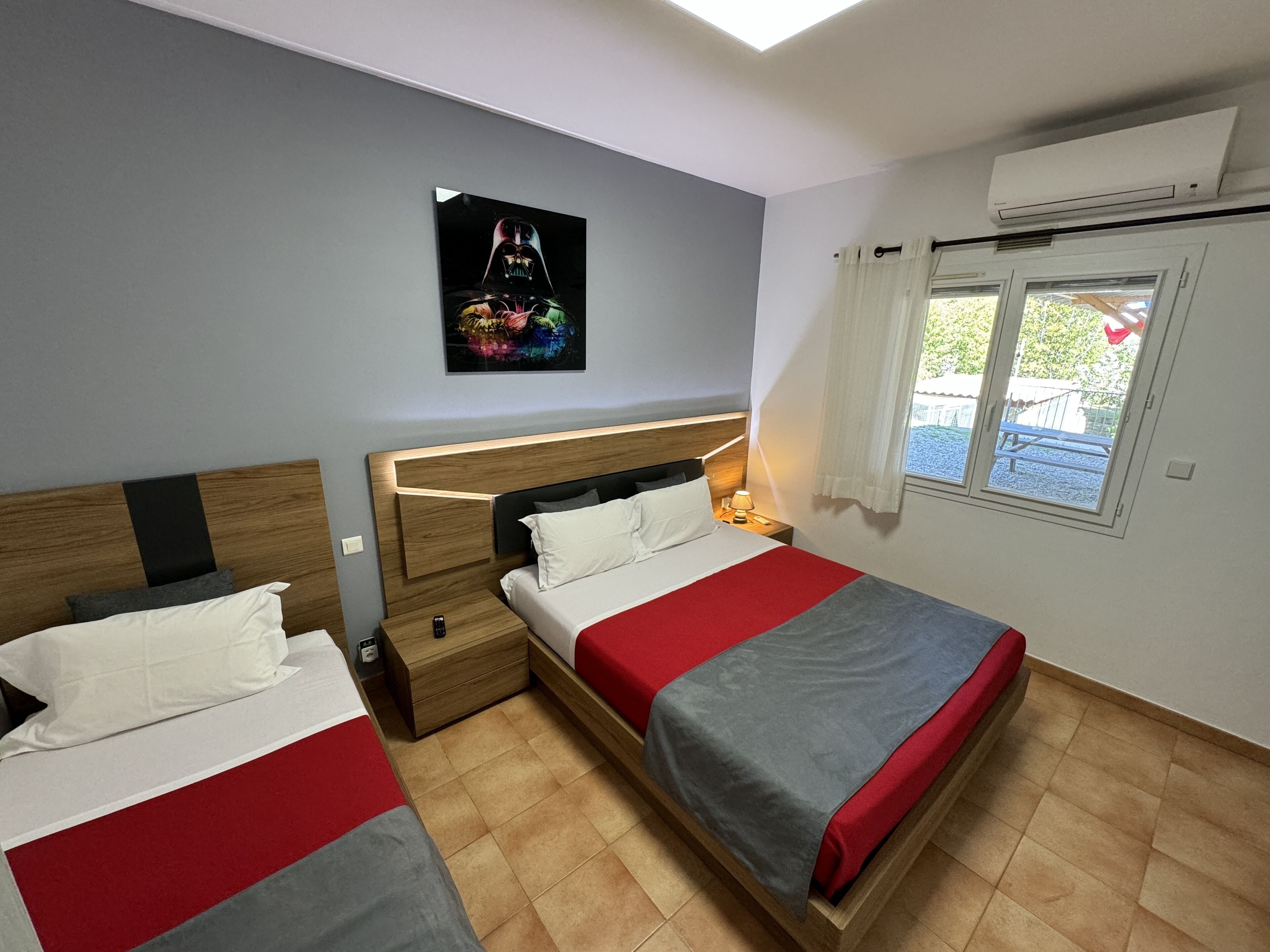 Habitación de hotel con dos camas, una lámpara en el techo, una ventana con cortinas y aire acondicionado instalado en la pared.