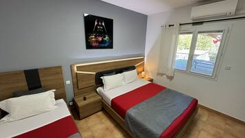 Habitación de hotel con dos camas, una lámpara en el techo, una ventana con cortinas y aire acondicionado instalado en la pared.