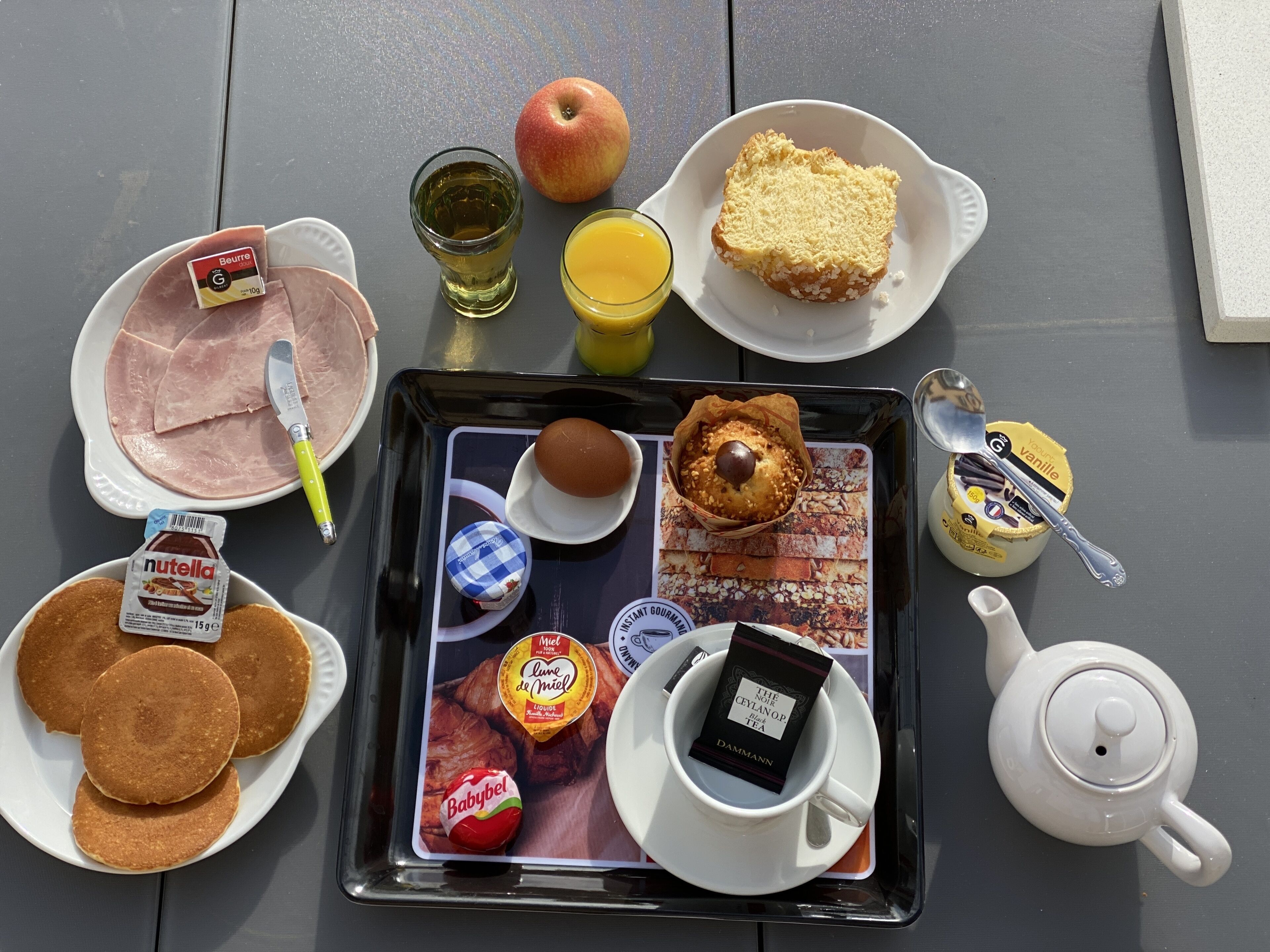 A tray with breakfast items including pancakes, ham, an apple, juice, and a muffin.
