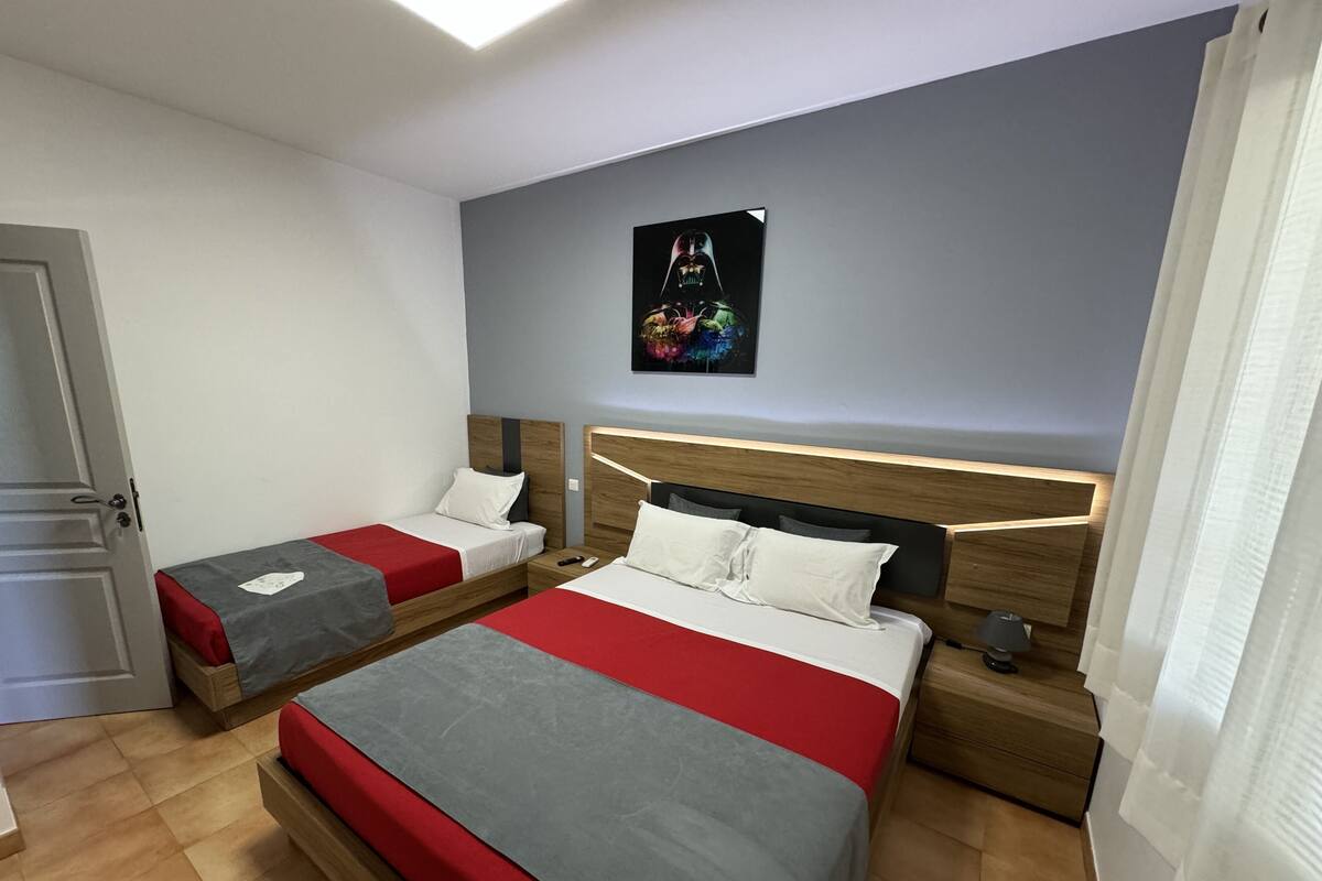 Een hotelkamer met twee bedden, een nachtkastje, een aan de muur hangend schilderij en een deur.