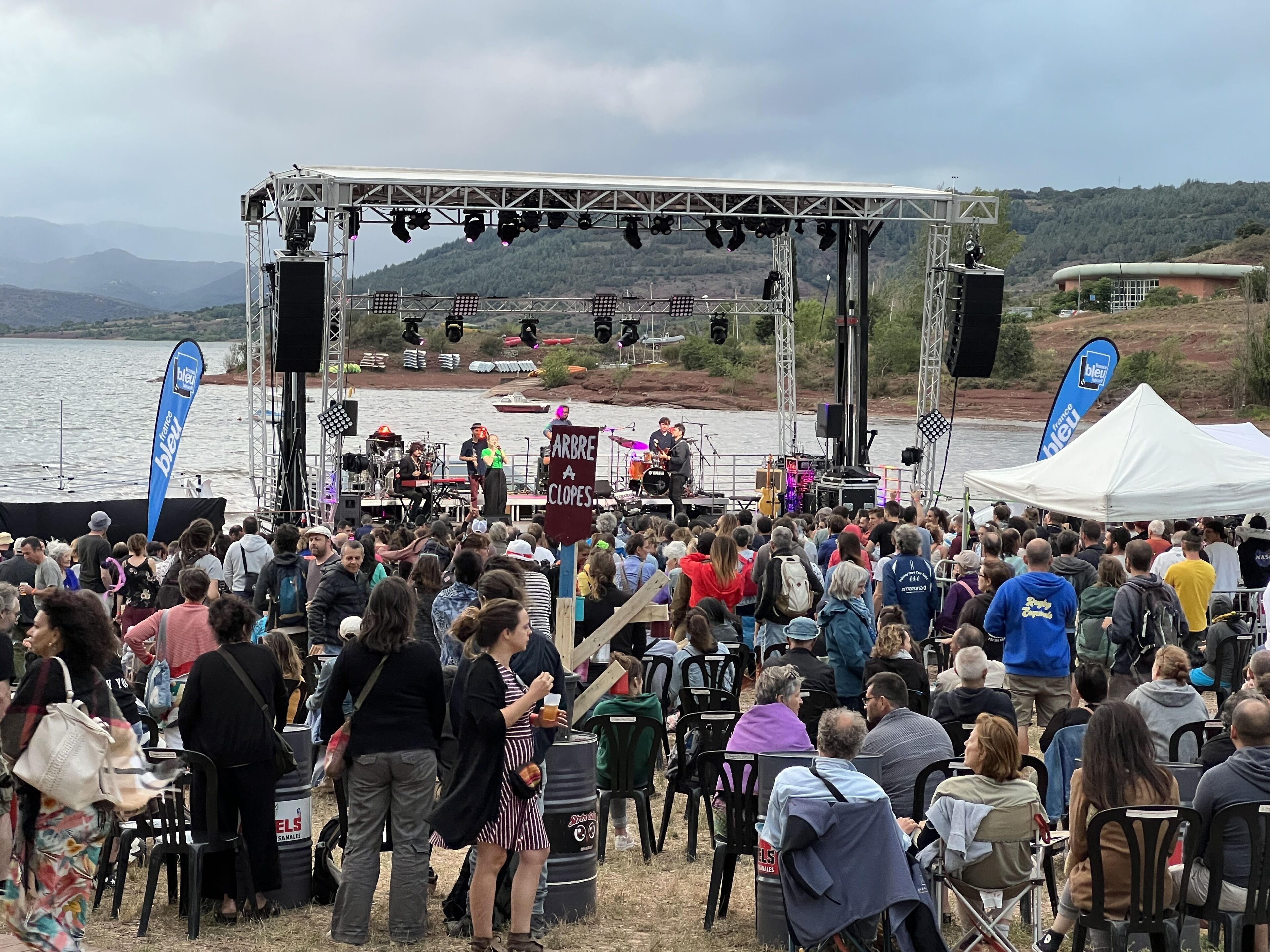 A stage with a band performing, surrounded by an audience seated on chairs.