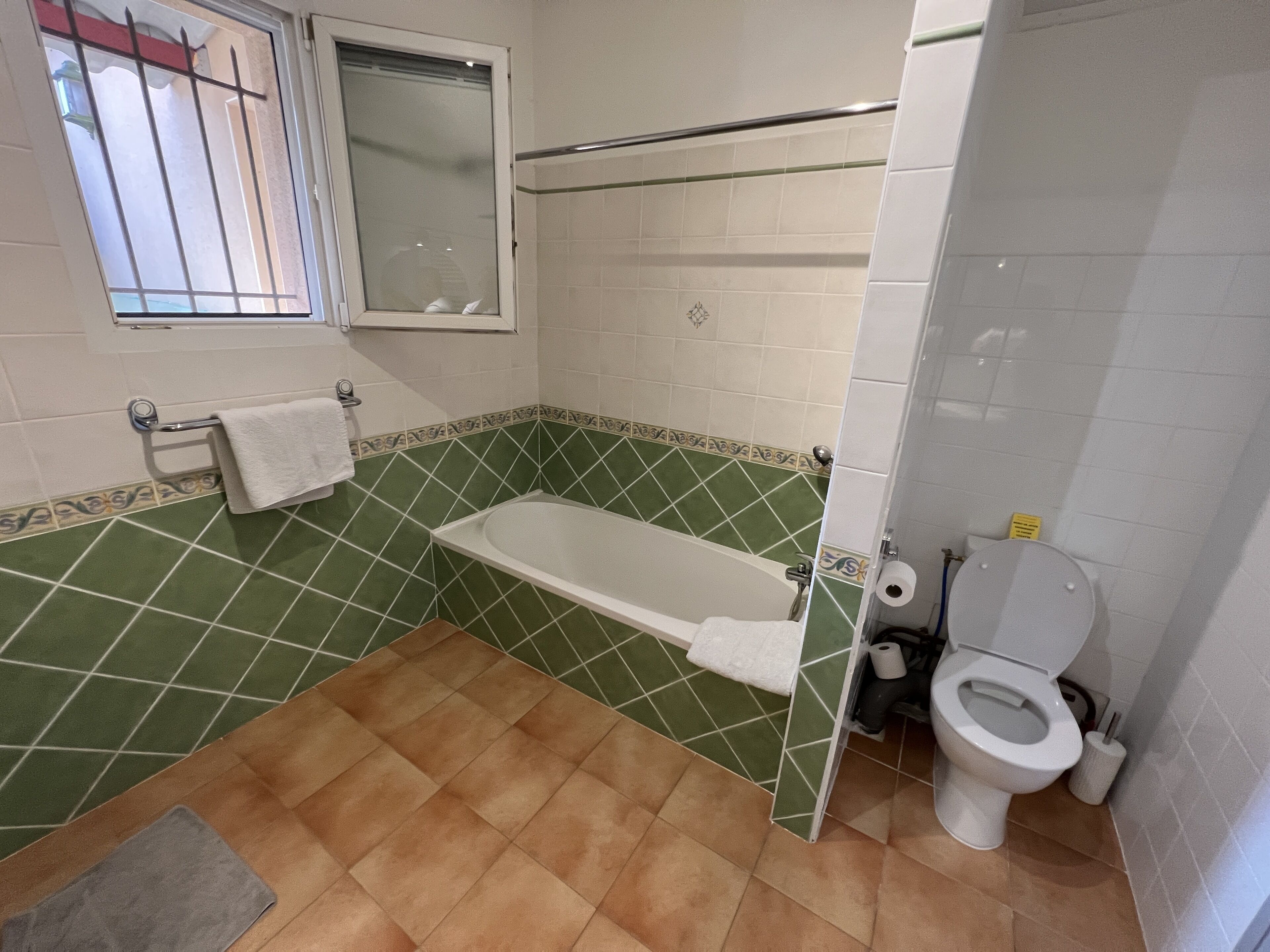 Un baño con bañera, inodoro y una ventana con barrotes.