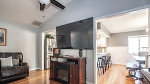 A modern living room with a flat-screen TV, a fireplace, and a dining area with bar stools. - Country  Clean  Cozy (Elizabethtown)