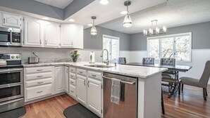 A modern kitchen with white cabinetry, stainless steel appliances, a marble island, and a dining area with a chandelier. - Country  Clean  Cozy (Elizabethtown)