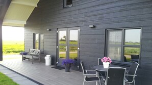 Un patio exterior moderno con terraza de madera, zona de estar con banco y sillas, y una planta en maceta.
