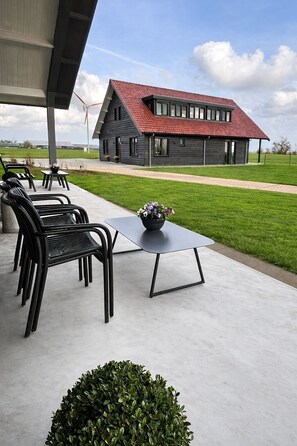 Un patio cubierto con mobiliario exterior, suelo de hormigón y vista a una casa de techo rojo.