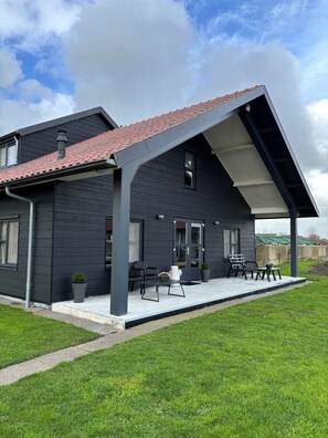 Una casa moderna con fachada oscura, techo de tejas rojas y un porche cubierto con mobiliario exterior.