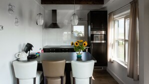 Una cocina moderna con una isla central, sillas blancas, una cafetera y un jarrón con girasoles.
