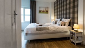 Un dormitorio con una cama grande, una mesita de noche con una lámpara, una ventana con cortinas y un cuadro colgado en la pared.
