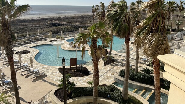 A resort pool area with multiple pools, palm trees, and a view of the beach.