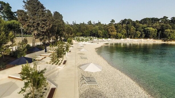 A beach with clear water, umbrellas, and a pathway leading to the shore. - Penthouse penthouse by the sea Rovinj, Residenza Federica (Rovigno)