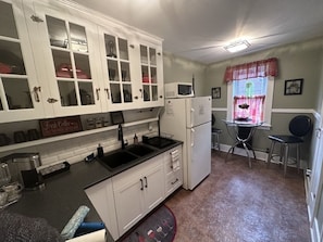 A compact kitchen with white cabinets, a black countertop, a refrigerator, and a dining area with a table and chairs.