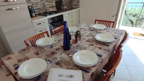 Comedor con una mesa dispuesta para cuatro, cocina al fondo y vistas al balcón.
