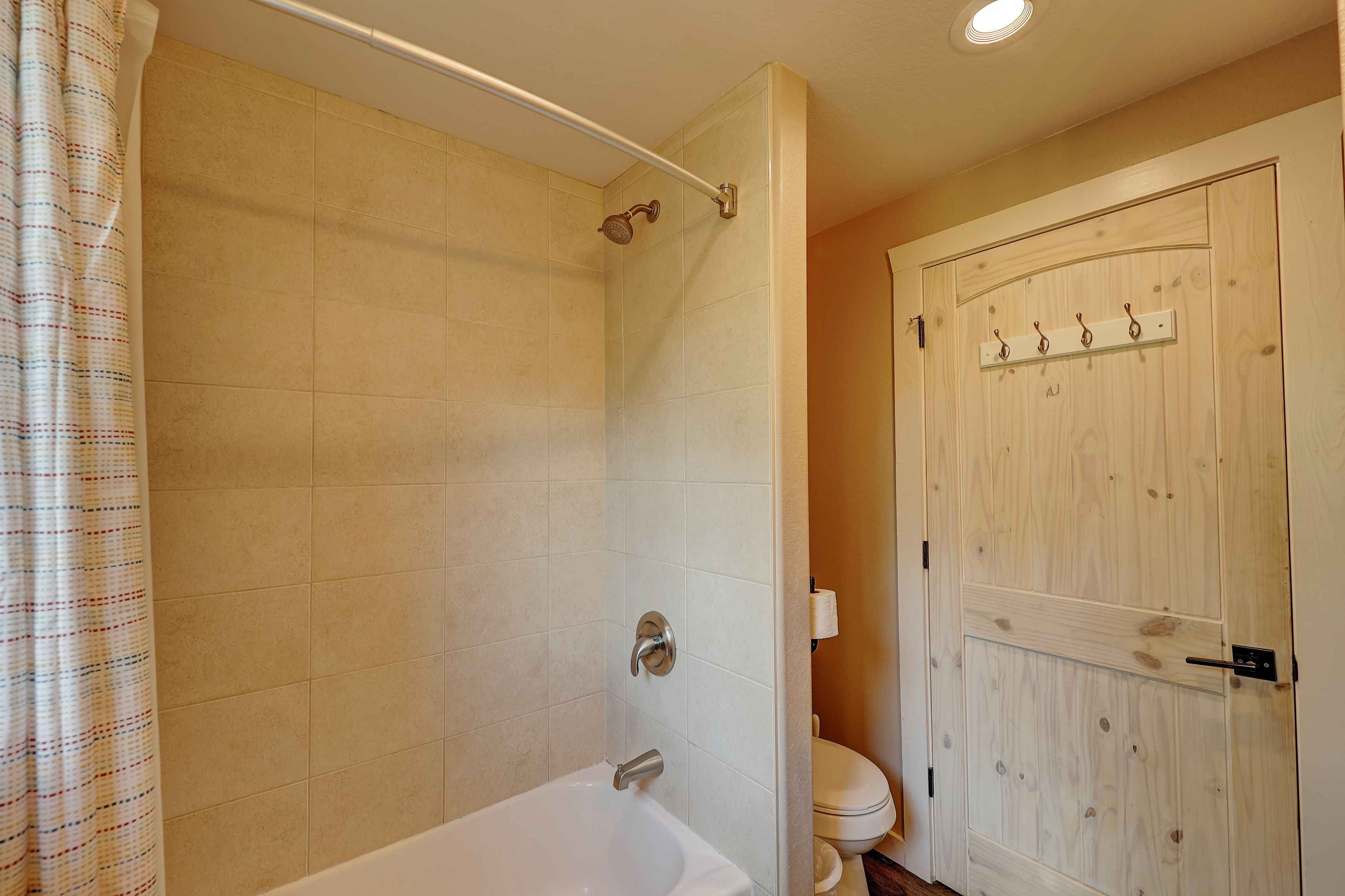 Une salle de bain avec douche, toilettes et une porte en bois dotée de crochets.