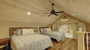 Een knus zolderkamer met twee bedden, een plafondventilator en uitzicht op de omgeving.