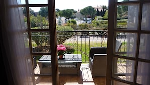 Un balcon agrémenté de meubles en osier, d’une plante en pot et offrant une vue sur un parking et des espaces verts.