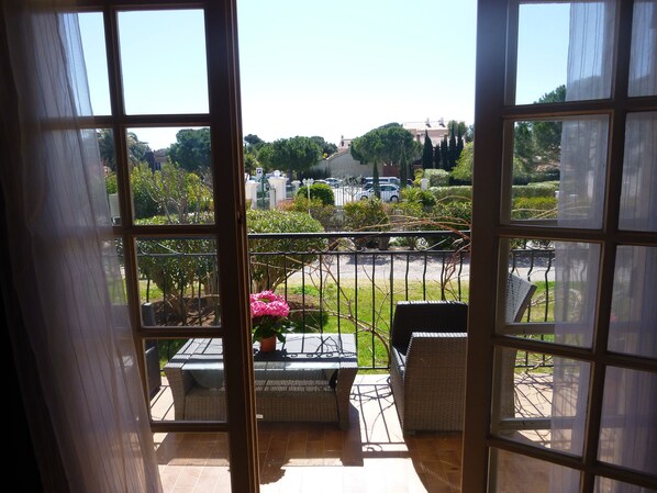 A balcony with wicker furniture, a potted plant, and a view of a parking area and greenery.