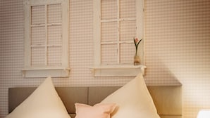 Una cama bien hecha con dos almohadas, una mesita de noche con lámpara y una ventana con diseño de cuadros.