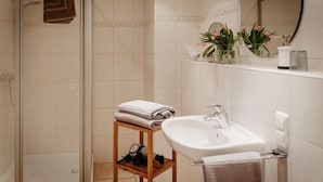Un baño con ducha, lavabo, espejo y estante con artículos de aseo.