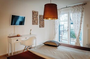 Un dormitorio con cama, escritorio, silla, televisor y ventana con cortinas.