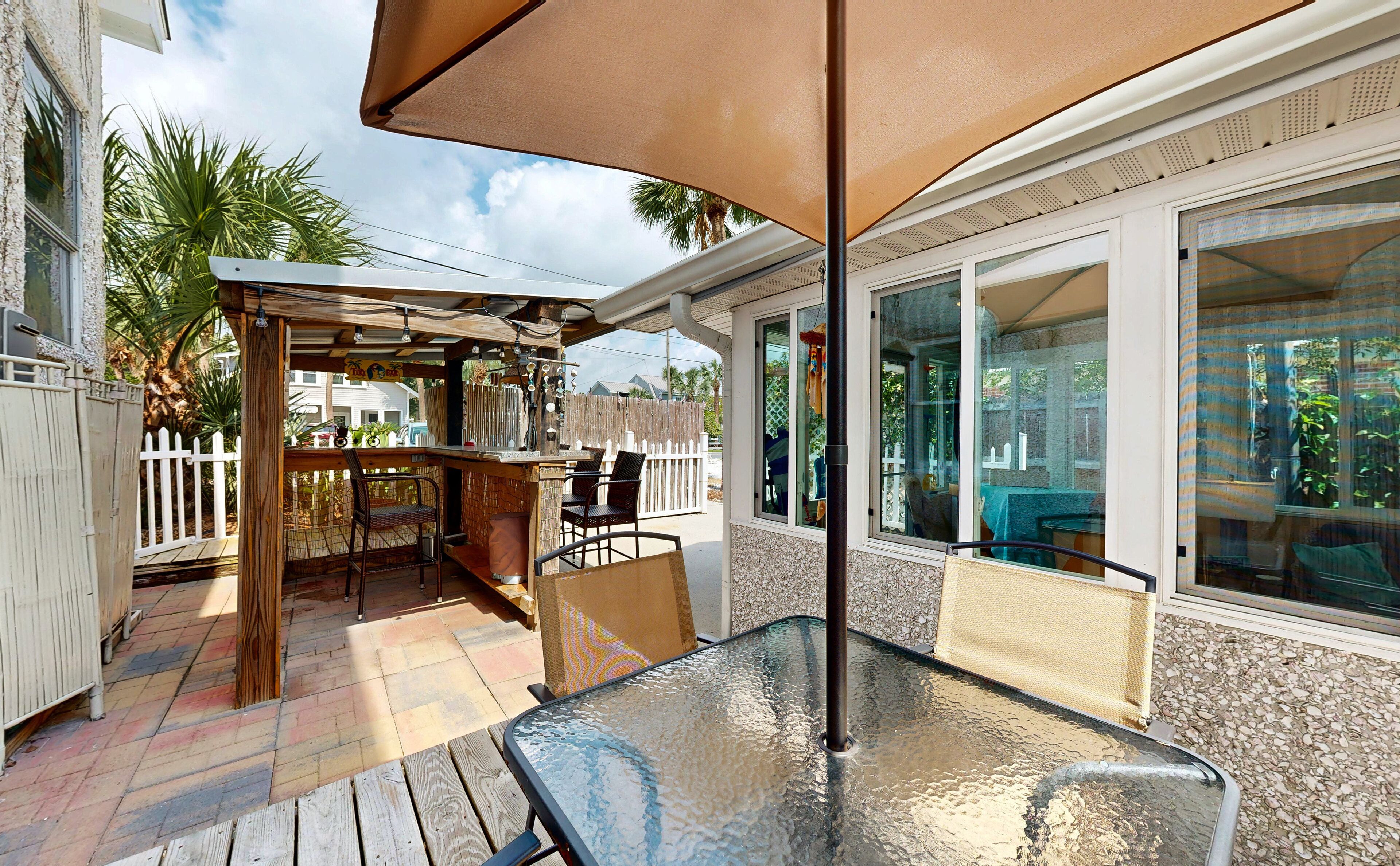 An outdoor patio with a glass table, chairs, and a wooden pergola.