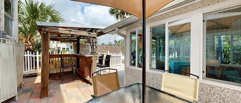 An outdoor patio with a glass table, chairs, and a wooden pergola.