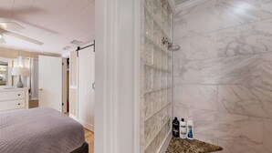 Une salle de bain avec une douche à parois de verre, des carreaux de marbre et des articles de toilette disposés sur un comptoir.