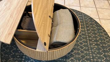 A round wooden bed with a built-in storage compartment, a patterned rug, and a white chair in the background.