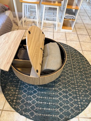 A round wooden bed with a built-in storage compartment, a patterned rug, and a white chair in the background.