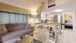 Un espace de vie compact comprenant un canapé, une petite table à manger avec des tabourets, un coin cuisine avec un réfrigérateur et une chambre avec un lit.