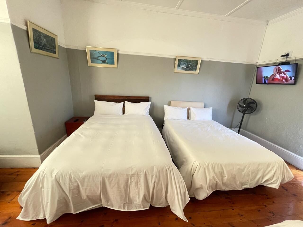 Quarto com duas camas, TV na parede e quadros enquadrados.