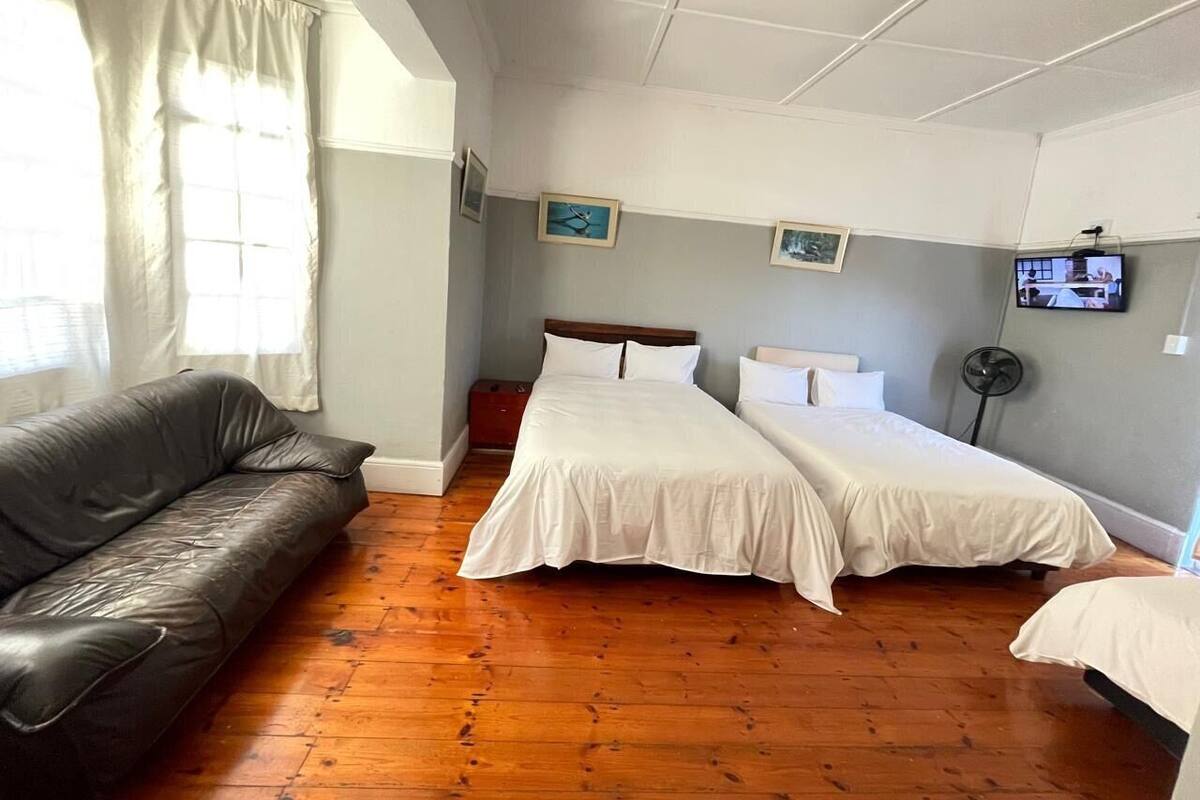 Een kamer met een houten vloer, een zwarte leren bank, twee eenpersoonsbedden met witte beddengoed, een klein tafeltje en een televisie aan de muur.