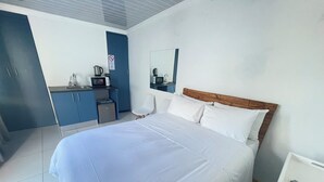 Una habitación de hotel con una cama grande, un escritorio, una silla, un microondas, una tetera y un refrigerador pequeño.