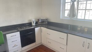 Una cocina con armarios blancos, encimera negra, estufa, microondas y ventana con cortinas.