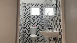 Un baño con pared de baldosas a cuadros, un inodoro, un lavamanos y una ducha.