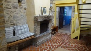 A stone-walled room with a fireplace, a bench with striped cushions, and a tiled floor. - Kerheol Pointe de la Torche - 200 m from the beach (Plomeur)