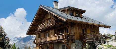 Eine Holzhütte mit mehreren Balkonen, einem Steinfundament und Blick auf Berge im Hintergrund.