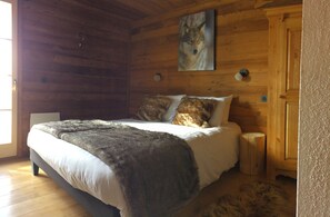 Een slaapkamer in een houten chalet, met een bed, een bont deken en een schilderij van een wolf aan de muur.